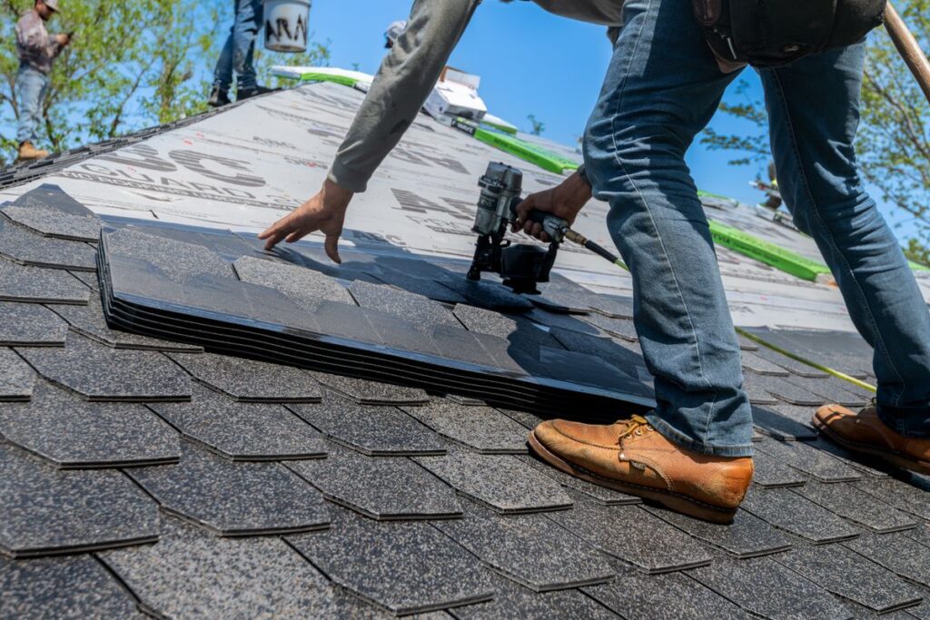 A roofer fastening asphalt shingles with a nail gun